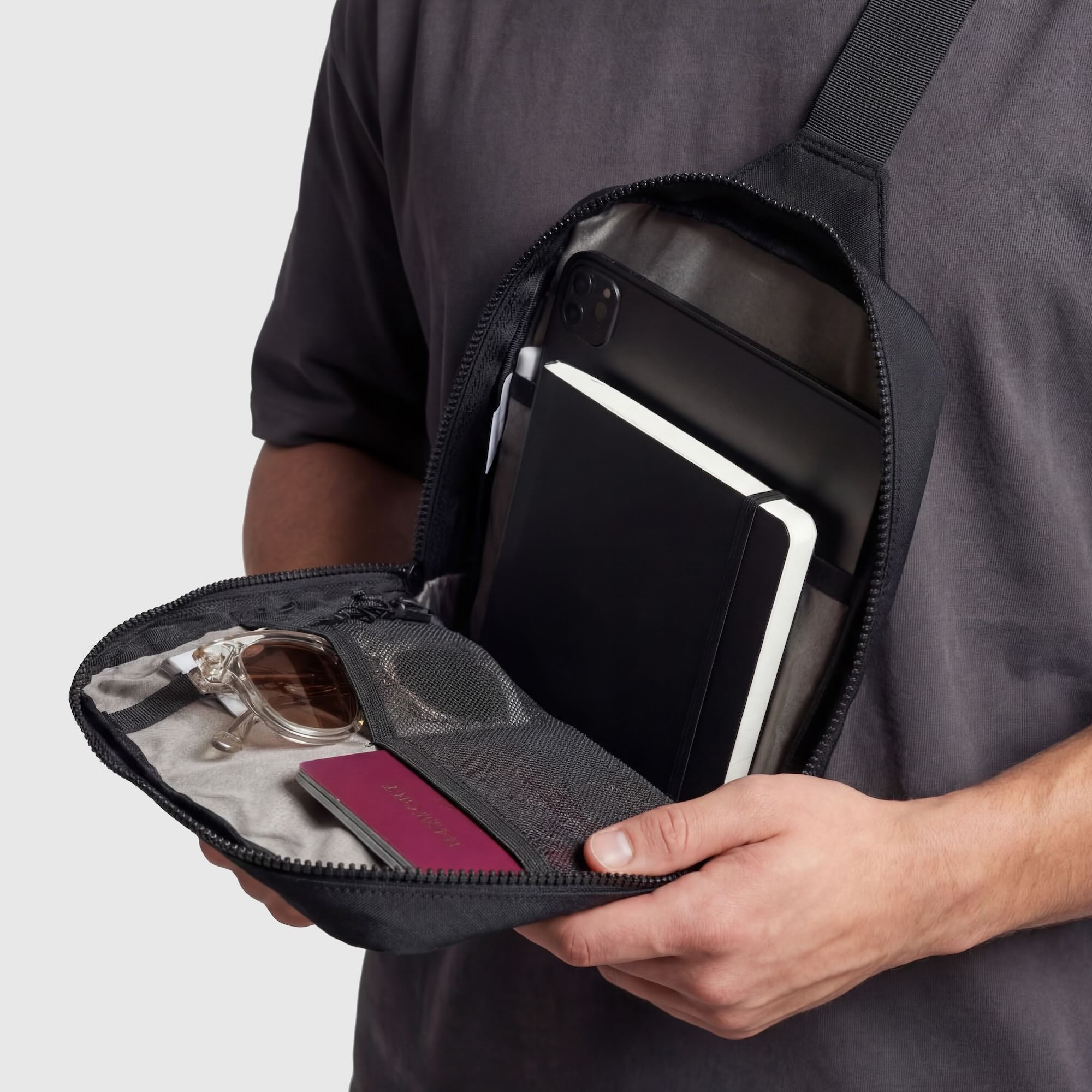Person holding a black crossbody bag with compartments open, showing items inside.