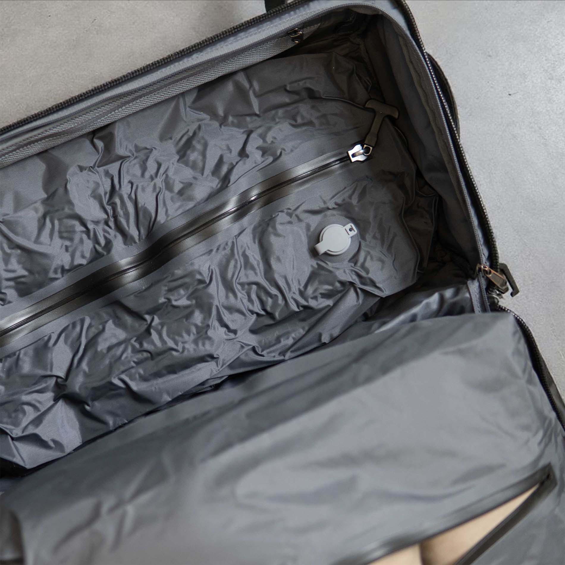 Open gray suitcase with crumpled gray packing cube inside on a light gray background