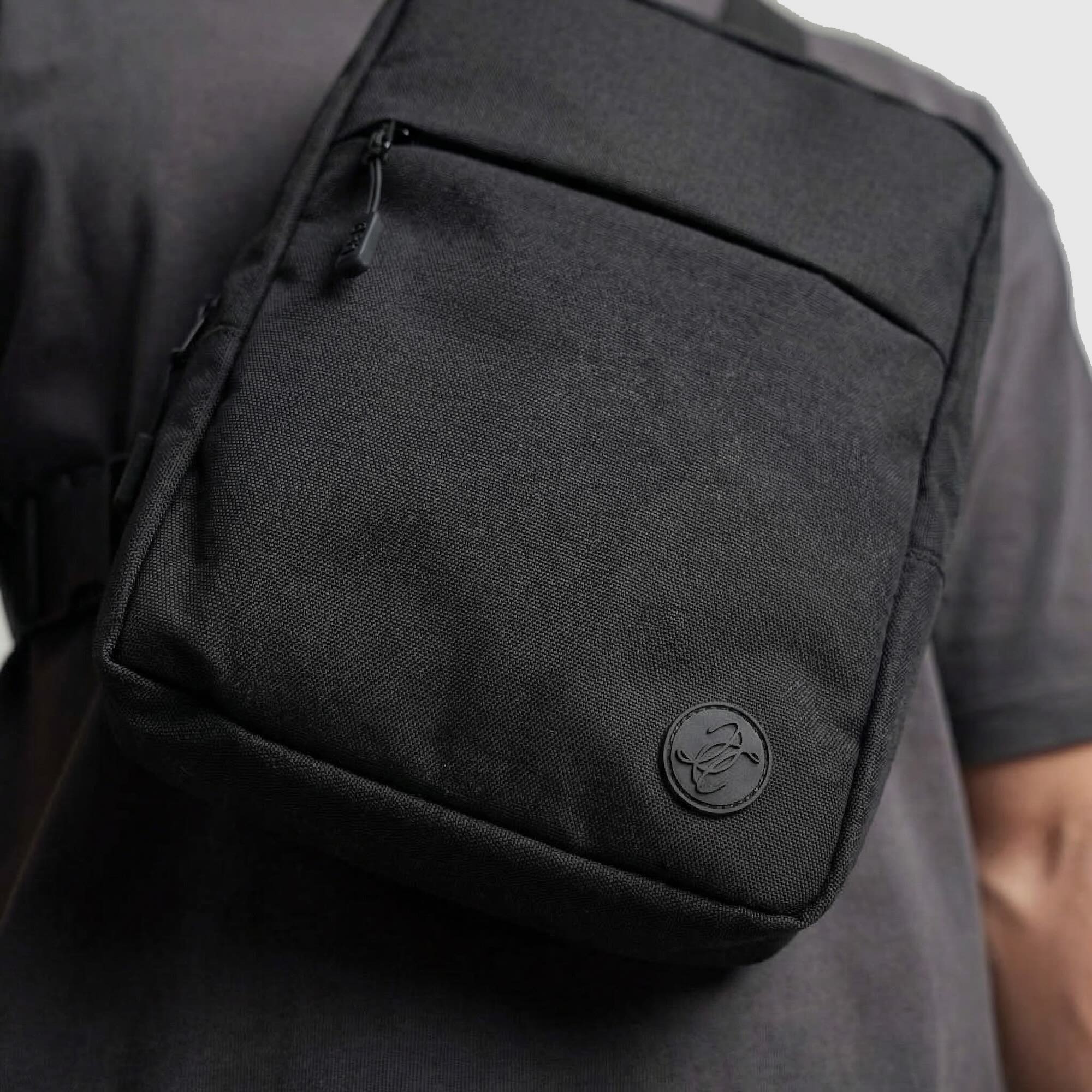 Black shoulder bag with a brand logo on a person wearing a dark shirt.