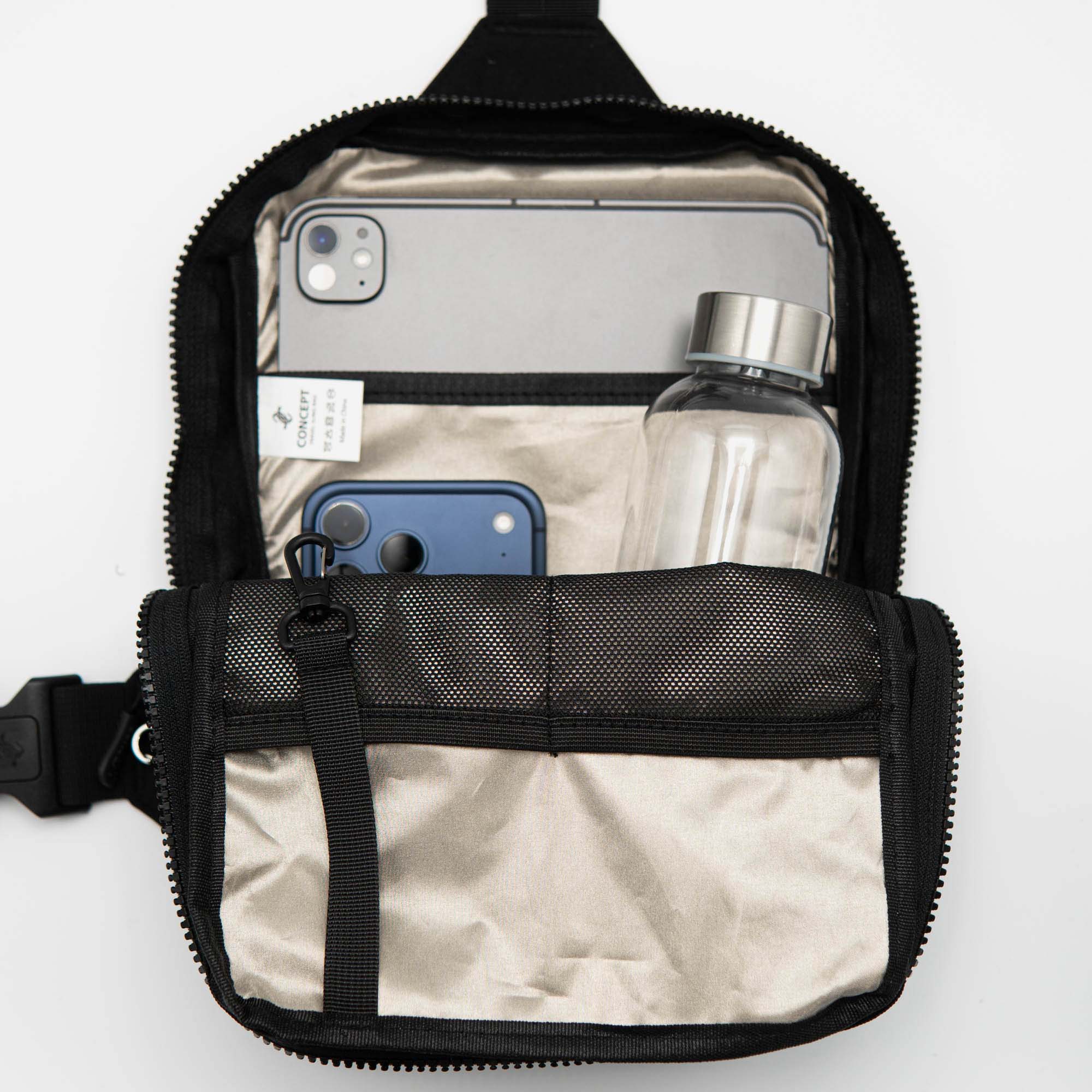 Black crossbody bag with phone, water bottle, and other items on a white background